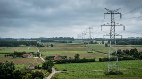 Pylônes électriques à haute tension traversant un paysage rural verdoyant sous un ciel nuageux